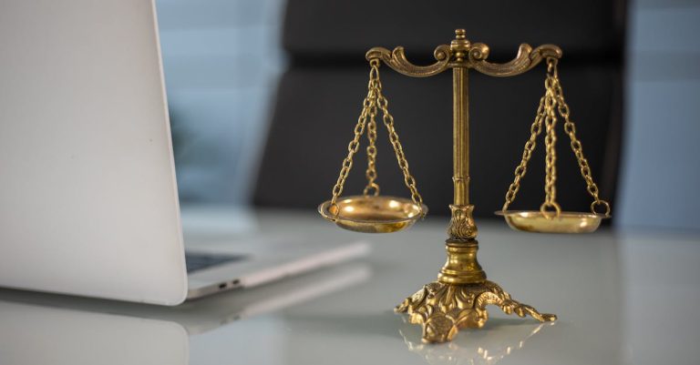 Golden justice scales on a desk beside a laptop, symbolizing law and balance.