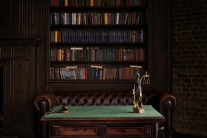 A classic study room with shelves of books, a gavel, and Lady Justice figurine on a green table.